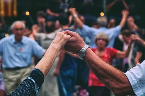 Two arms holding hands with a group of people in the background holding hands in a circle